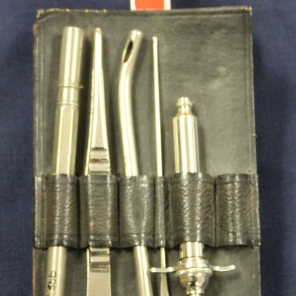 [Ada J. Ross Chatelaine.] Black leather case hung from a Red Cross belt clip containing a broken thermometer, tissue forceps, probe, metal suction tip, and a metal hypodermic syringe.